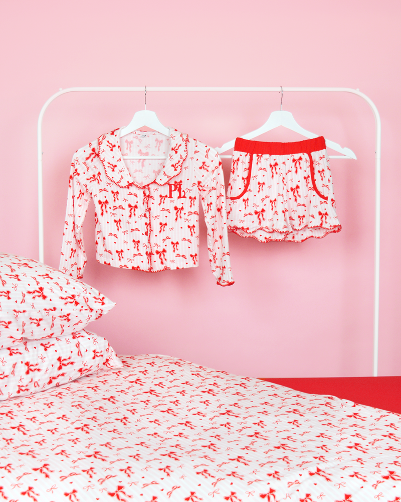 Rosa-weiß gestreifte Mädchen-Pyjamashorts von P.Louise mit Weihnachtsschleife auf Kleiderbügeln in einem rosafarbenen Schlafzimmer mit passender Bettwäsche