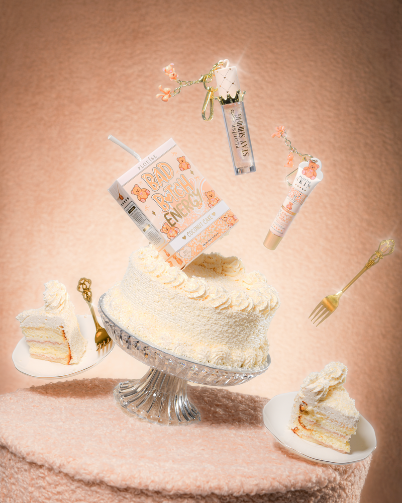Ein Kuchen auf einem Teddy-Stofftisch mit einem P.Louise Teddy Glitter Bad Bitch Energy Lip Duo in Kokosnuss-Kuchenform, das einen Lippenpflegemittel und Lippenöl enthält, das um den Kuchen schwimmt