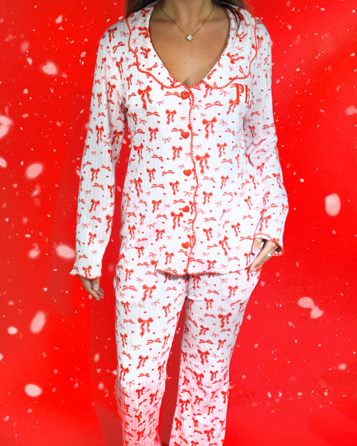 Aufnahme des Körpers einer Frau, die einen festlichen rosa-weiß gestreiften Pyjama mit roten Schleifenmotiven vor einem roten Hintergrund und Schneeflocken trägt