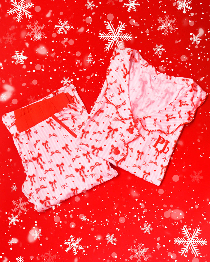Paar rosa-weiß gestreifte Pyjamas mit roten festlichen Schleifenmustern auf einem roten Hintergrund mit Schneeflocken