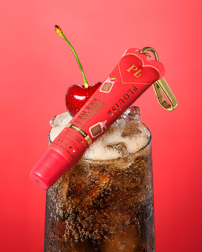 Roter, nach Kirsch-Cola duftender, getönter Lippen-Conditioner zum Schutz Ihres Schmollmunds mit goldenem Clip auf einem Glas Kirsch-Cola mit einer Kirsche