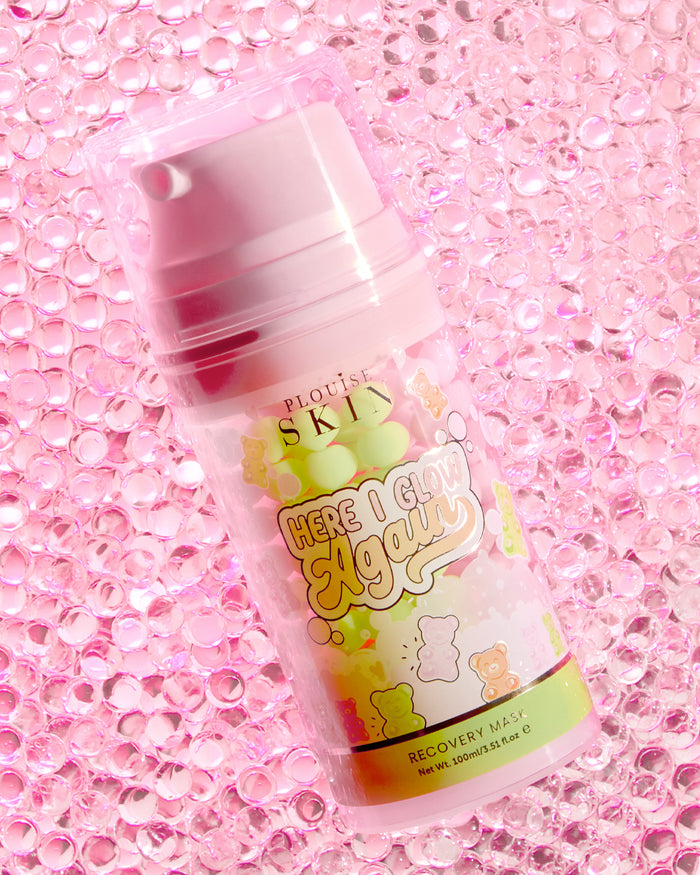 Eine Flasche P.Louise Here I Glow Again Recovery Mask mit dem Duft von Bonbonbären und einem rosa-grünen Etikett mit Illustrationen von Bonbonbären auf einem rosa glitzernden Hintergrund.