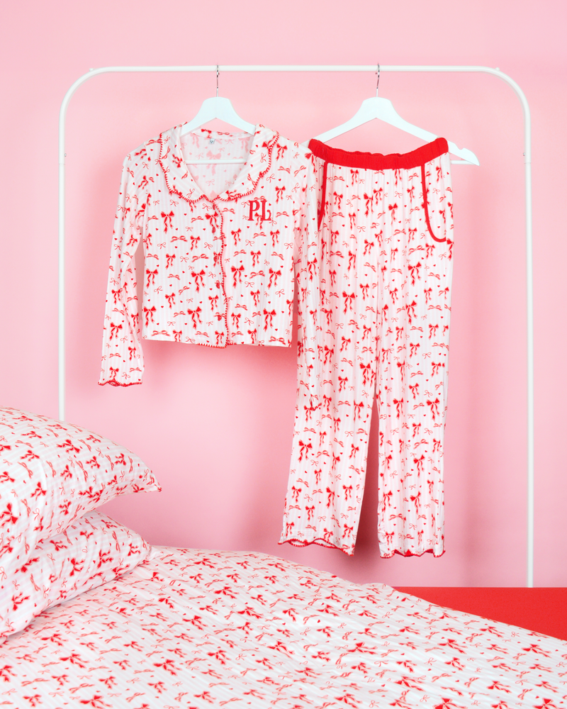 Mädchen-Pyjama-Set mit weihnachtlicher Schleife von P.Louise mit durchgehend rotem Schleifenmuster auf rosa und weißen Streifen, die an Kleiderbügeln in einem rosafarbenen Schlafzimmer mit passender Bettwäsche hängen