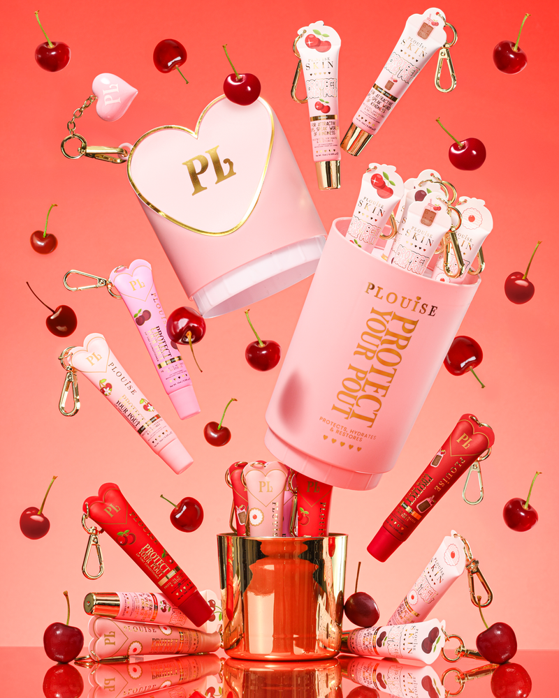 Pink XL Protect Your Pout Geschenkset, das geöffnet ist, umgeben von Kirschen und rosa und roten Lippenpflegemitteln auf einem rosa Hintergrund