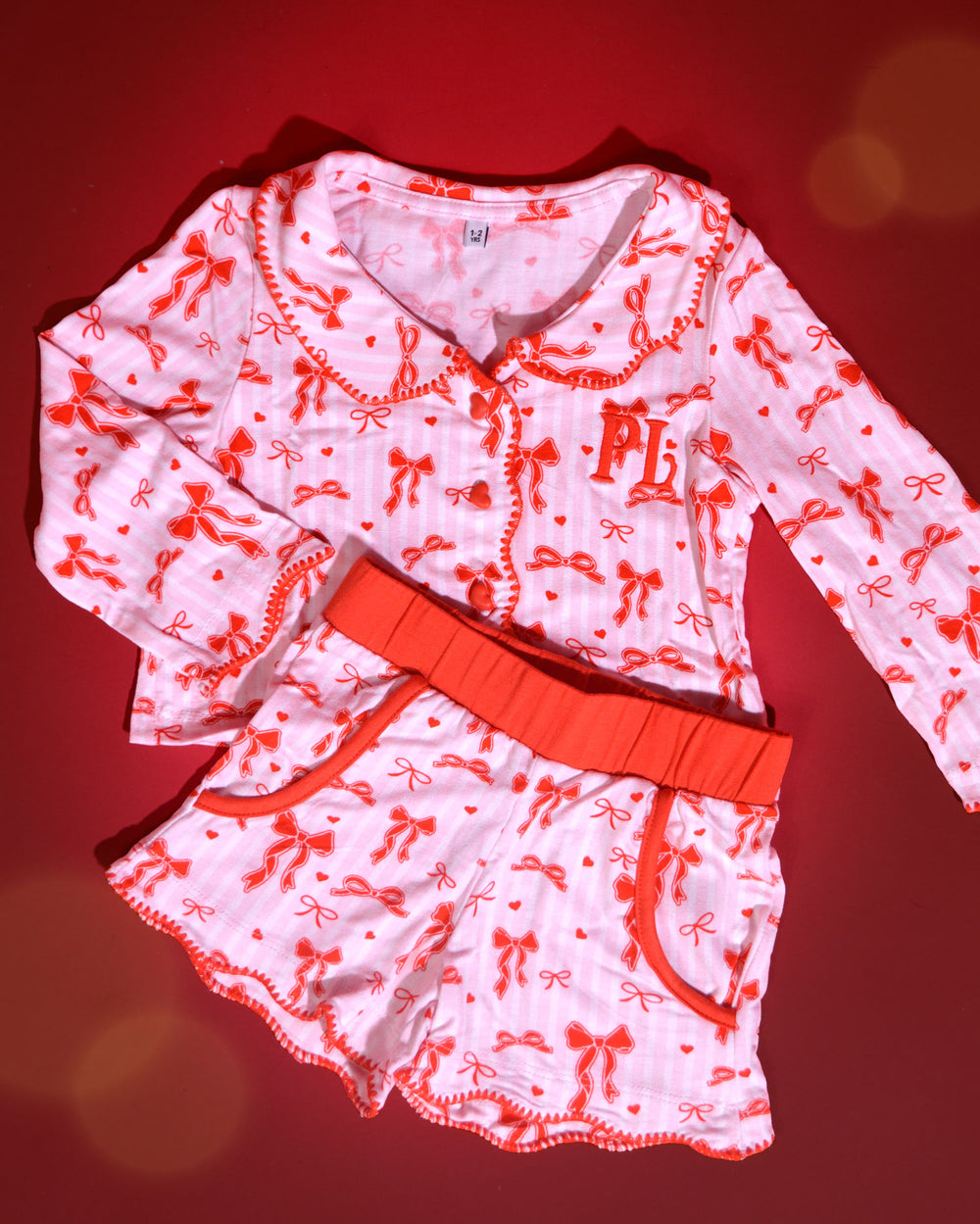 Set aus rosa-weiß gestreiften Kinder-Weihnachtspyjamas mit roten Schleifenmotiven vor rotem Hintergrund