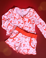 Set aus rosa-weiß gestreiften Kinder-Weihnachtspyjamas mit roten Schleifenmotiven vor rotem Hintergrund