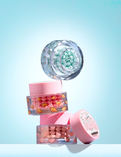 Drei kleine Gläser mit bunten Vitamin-C-Kapseln in einem Gel auf hellblauem Hintergrund