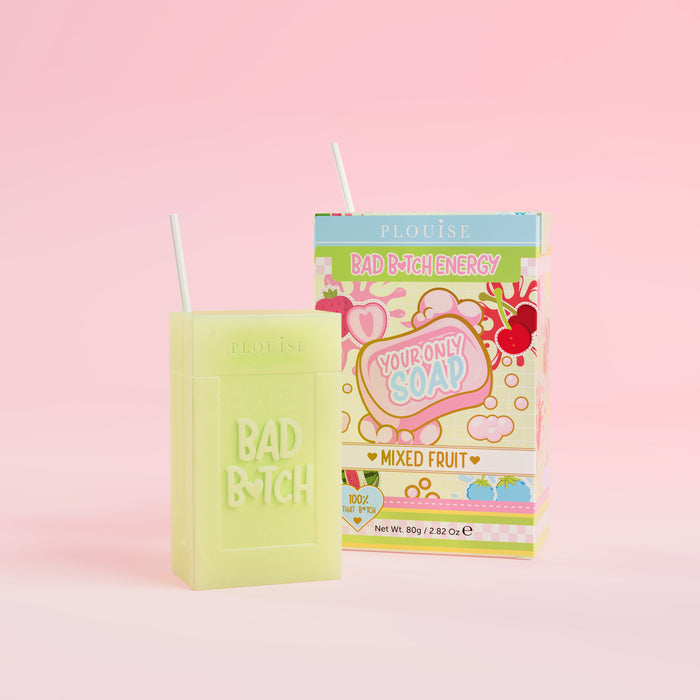 Ein grünes Stück Seife mit der Gravur „Bad Bitch“, begleitet von einer bunten Saftschachtel mit der Aufschrift „Mixed Fruit“, präsentiert auf einem rosa Hintergrund.