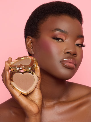 A woman holding a P.Louise heart-shaped compact containing an under-eye brightening and blurring pressed powder