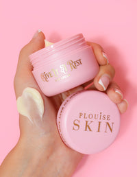 Eine Person hält ein rosafarbenes Glas Augencreme „P.Louise Give It A Rest“ mit abgenommenem Deckel in der Hand, auf dem der Produktname und die Marke zu sehen sind.