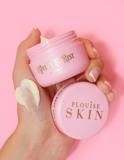 Eine Person hält ein rosafarbenes Glas Augencreme „P.Louise Give It A Rest“ mit abgenommenem Deckel in der Hand, auf dem der Produktname und die Marke zu sehen sind.